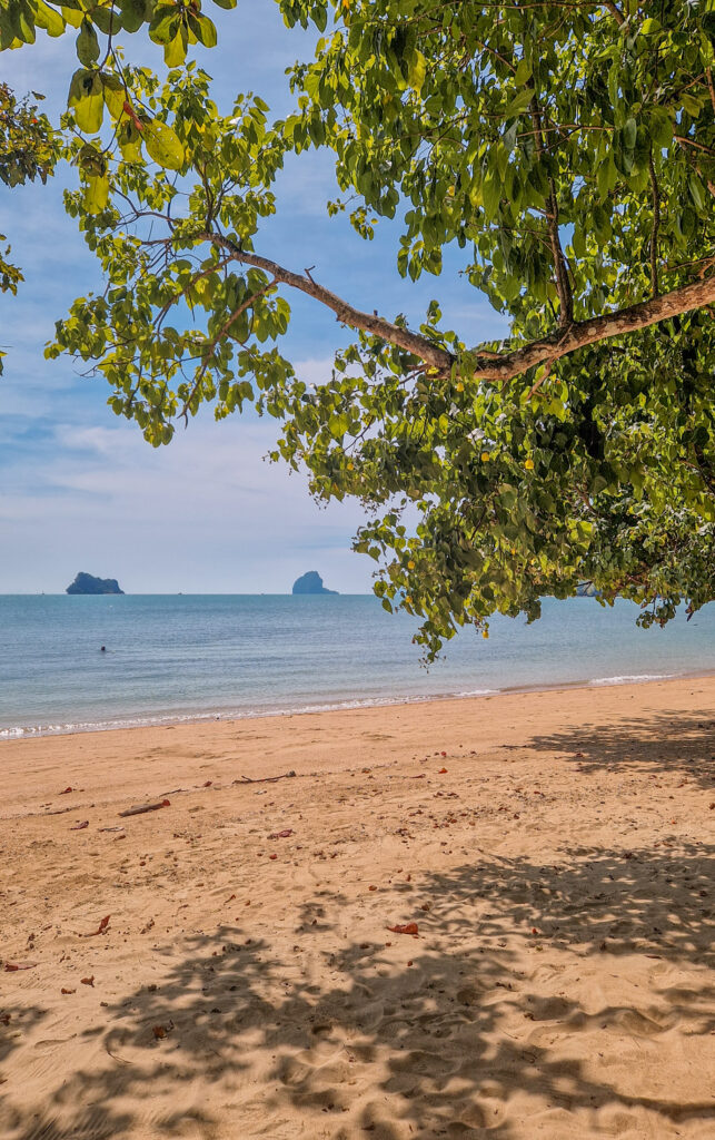 Einsamer Sandstrand auf Koh Yao Noi mit Baumschatten und Kalksteinfelsen im Meer