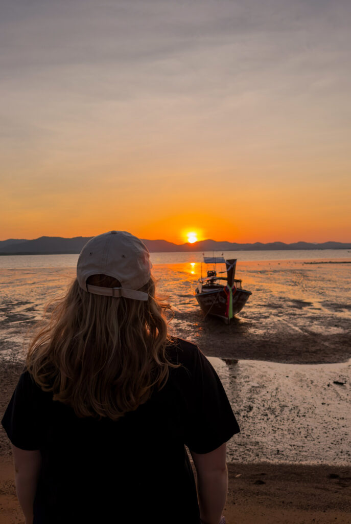Frau geniesst den Sonnenuntergang auf Koh Yao Noi mit Blick auf Longtailboot und Meer